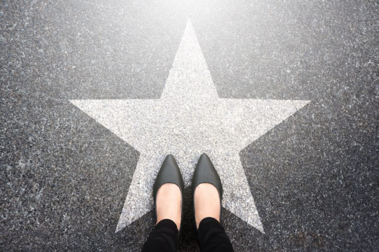 Black high heel shoes standing on silver star symbol on walk of fame.