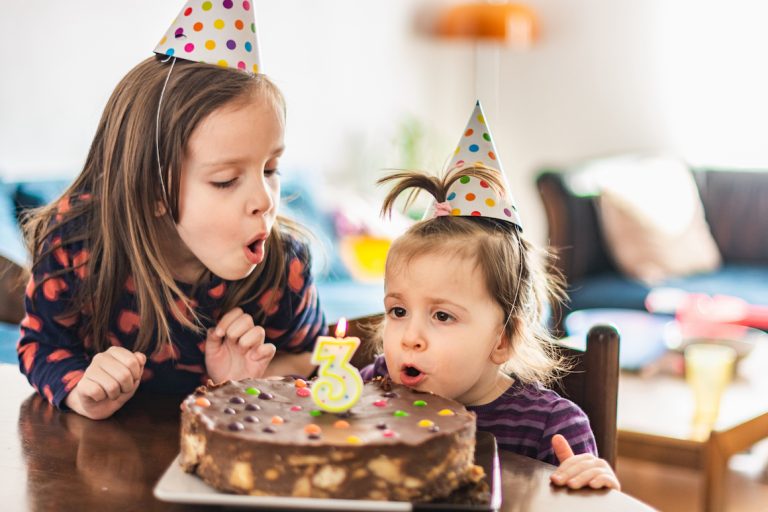 Two young girls blowing out birthday candle at third birthday party