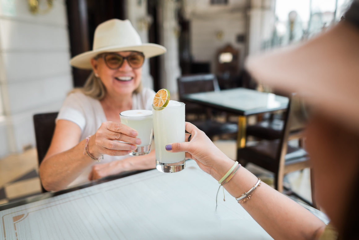 A happy older woman toasts her lemonade glass with a friend